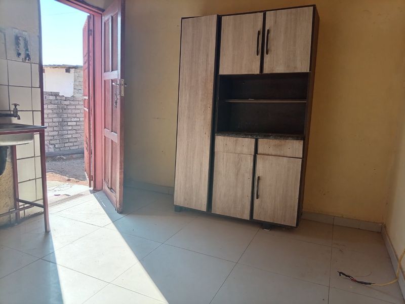 A basic kitchen area featuring tiled flooring, a sink, and a standalone storage unit, with direct access to the exterior.