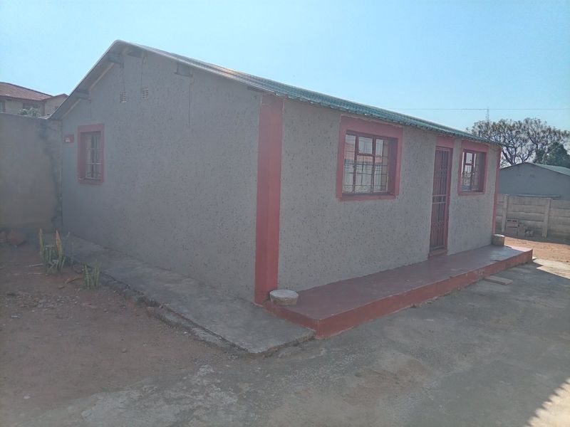 A view of the front exterior of a single-story house featuring painted masonry walls, a metal roof, and security bars on the windows.