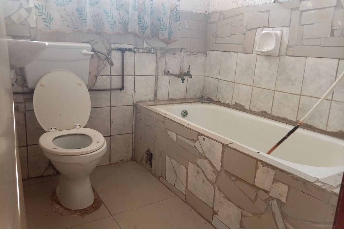 A dated bathroom featuring a bathtub, toilet, and basin with significant tile damage and exposed plumbing, requiring renovation and modernization.