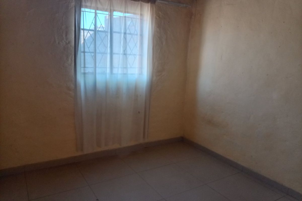 An empty bedroom featuring tiled flooring and a window with security bars, presenting a blank canvas for potential renovation or interior design updates.