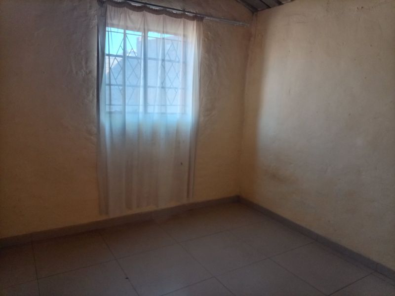 An empty bedroom featuring tiled flooring and a window with security bars, presenting a blank canvas for potential renovation or interior design updates.