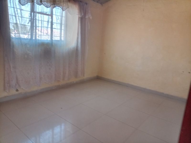 A vacant bedroom featuring tiled flooring and a window fitted with security bars, offering a blank canvas for potential interior updates.