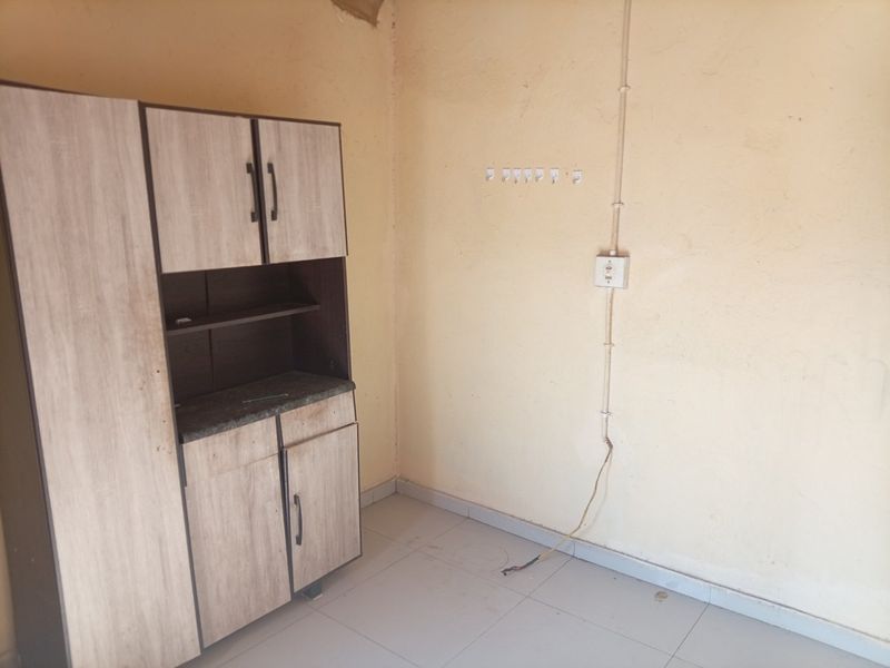 A small, empty kitchen area featuring basic built-in cabinetry, tiled flooring, and exposed electrical wiring on the wall.