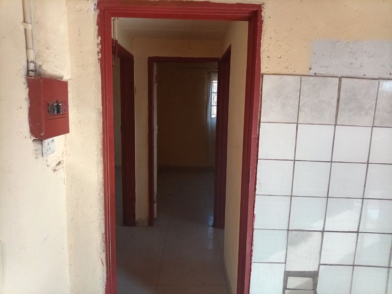 A narrow interior hallway featuring exposed electrical infrastructure, tiled wall sections, and multiple doorways leading to adjacent rooms, requiring cosmetic refurbishment.