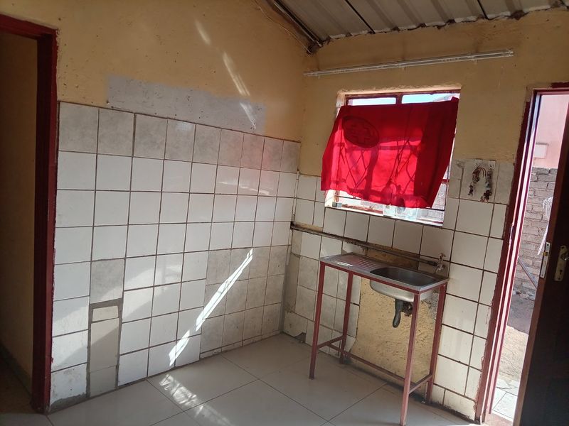 A basic kitchen area featuring a stainless steel sink, tiled splashback, and tiled flooring, currently requiring significant renovation and cosmetic repairs.