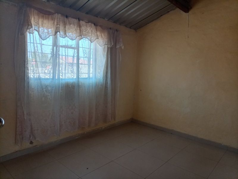An empty bedroom featuring tiled flooring, security bars on the window, and an exposed corrugated metal ceiling.