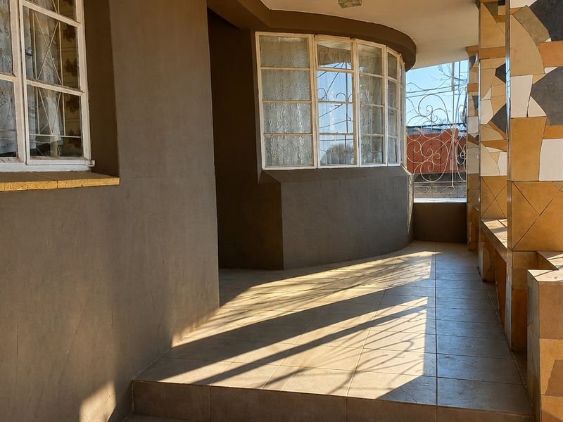 A covered patio area featuring tiled flooring, decorative tiled pillars, and a curved window facade with wrought iron security features.