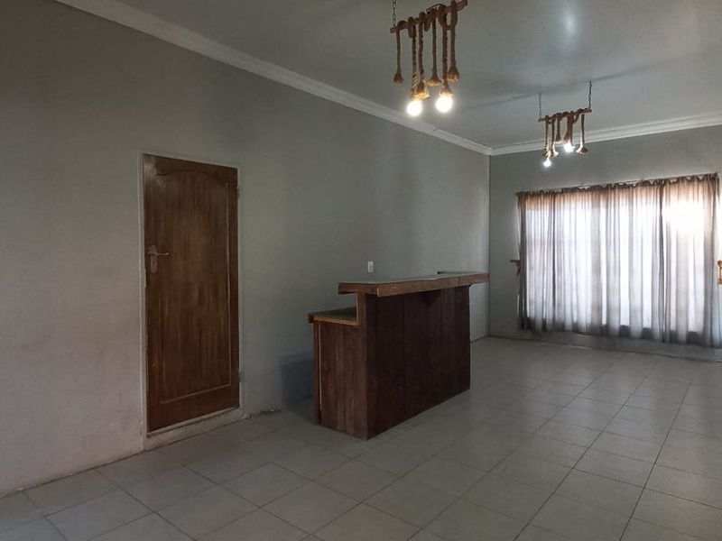 An open-plan living area featuring tiled flooring, a built-in timber bar counter, and large windows with curtains.