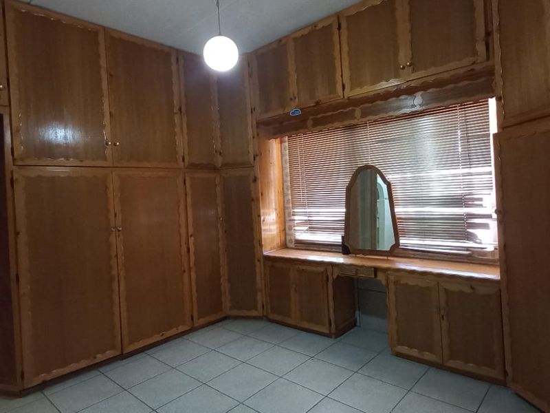 A bedroom featuring extensive built-in wooden cabinetry, a built-in vanity unit, tiled flooring, and window blinds.