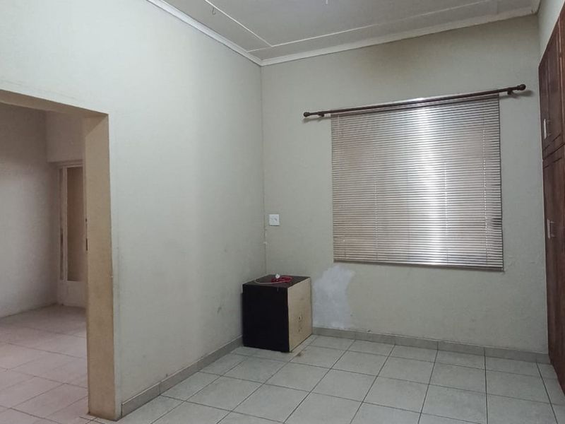 A vacant bedroom featuring tiled flooring, built-in wooden cupboards, and venetian blinds, requiring minor cosmetic updates to the wall finishes.