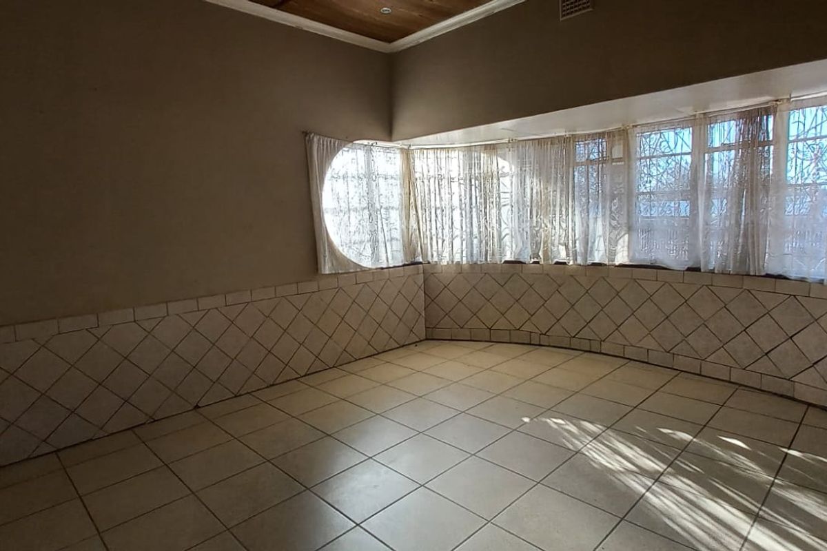 An empty living room featuring tiled flooring, tiled wall wainscoting, and a large bay window with security bars.