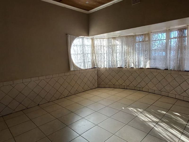 An empty living room featuring tiled flooring, tiled wall wainscoting, and a large bay window with security bars.