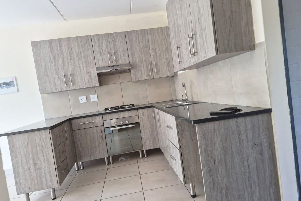Modern kitchen featuring wood-grain cabinetry, granite countertops, built-in oven, gas hob, and extractor fan, finished with neutral tiled splashbacks and flooring.