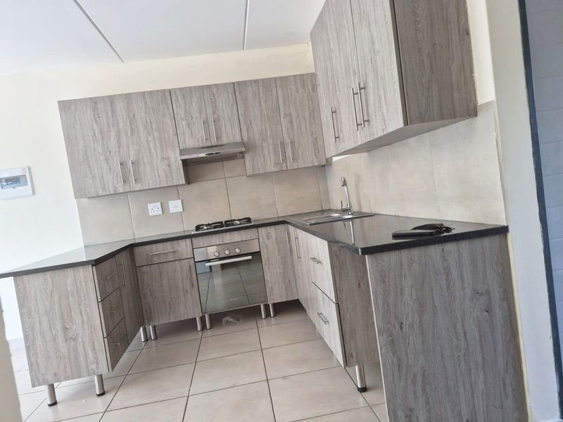 Modern kitchen featuring wood-grain cabinetry, granite countertops, built-in oven, gas hob, and extractor fan, finished with neutral tiled splashbacks and flooring.