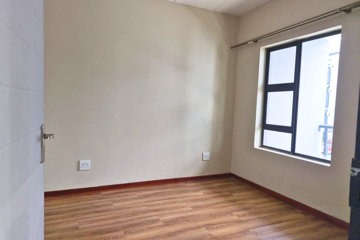 A clean, empty bedroom featuring modern laminate flooring, neutral wall finishes, and an aluminium-framed window providing natural light.