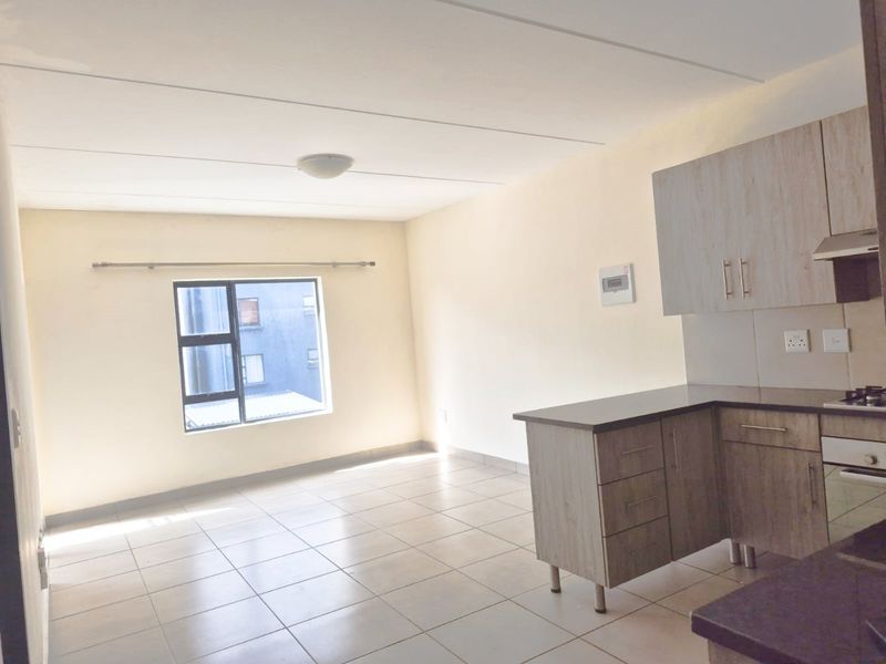 An open-plan living and kitchen area featuring neutral ceramic floor tiles, modern wood-look cabinetry, and a built-in oven with extractor fan.