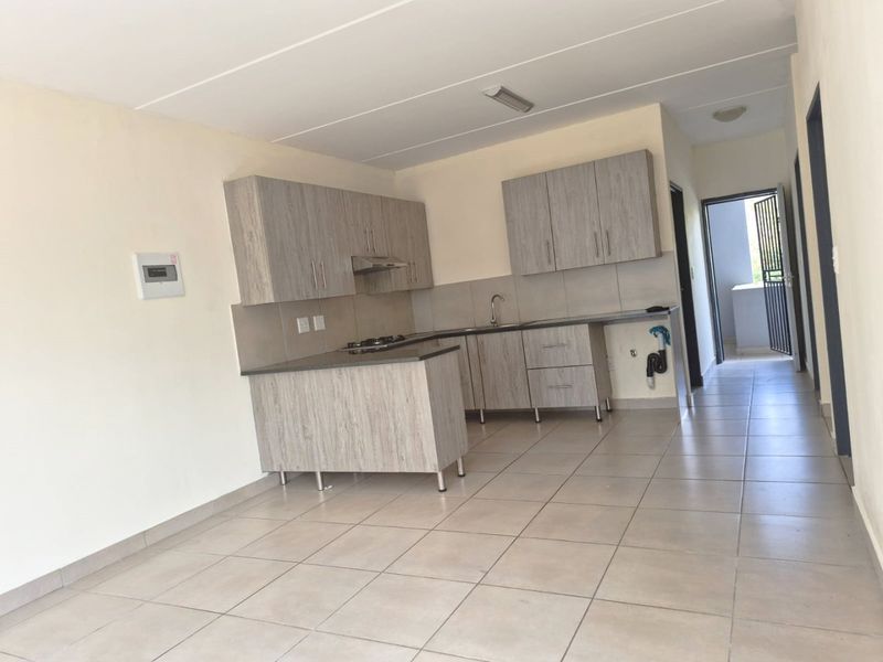 A functional, empty kitchen featuring light wood-grain cabinetry, laminate countertops, a gas hob, and tiled flooring, ready for personalization.