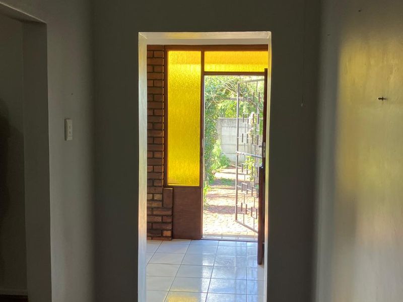 An interior entry hallway featuring timber flooring, leading through a doorway with a yellow glass sidelight and security gate to the exterior.