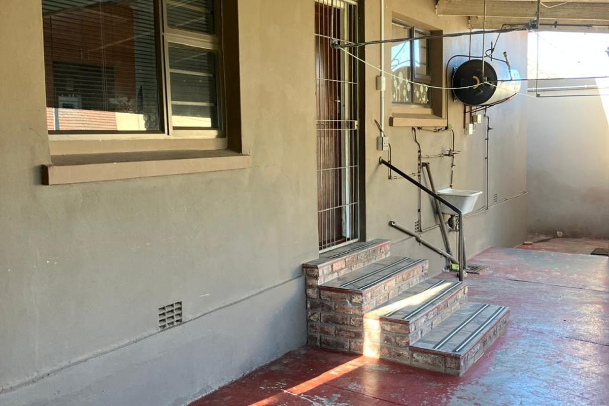 Rear exterior area featuring a covered patio with brick steps, an external wash basin, and an exposed electric geyser.