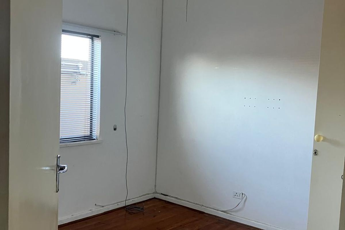 An empty bedroom featuring original timber flooring, a ceiling fan, and a window with venetian blinds, requiring minor cosmetic repairs to walls.