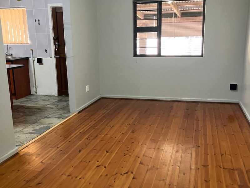 An open-plan living area featuring polished timber flooring, neutral walls, and a view through to the adjacent kitchen area.