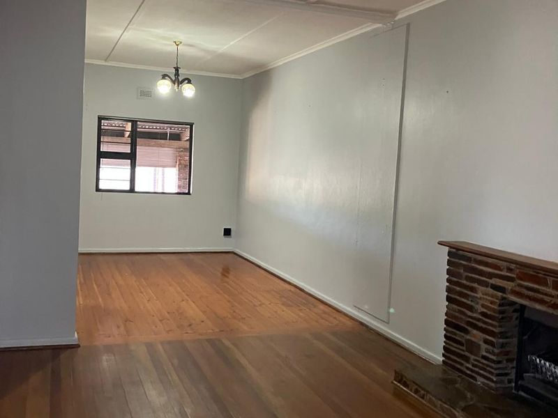 Spacious living area featuring polished timber flooring, a classic brick fireplace, and neutral wall finishes, offering a versatile blank canvas for interior design.