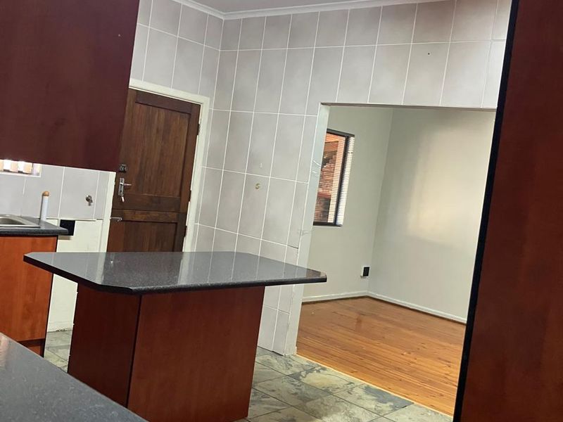 A functional kitchen space featuring built-in cabinetry, dark countertops, and tiled finishes, leading into an adjacent room with timber flooring.