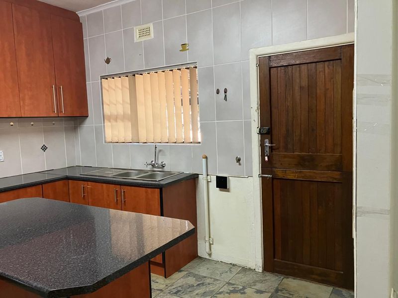 A functional kitchen featuring wooden cabinetry, granite countertops, a double basin sink, and tiled backsplash, with direct access to an exterior wooden door.