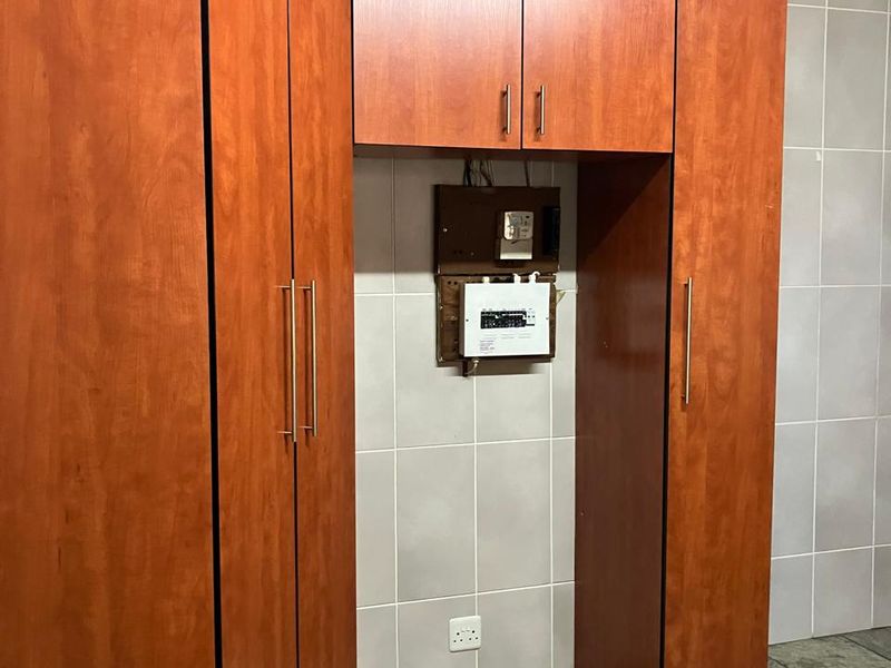 A utility area featuring built-in wooden cabinetry, tiled walls, and flooring, with an exposed electrical distribution board.