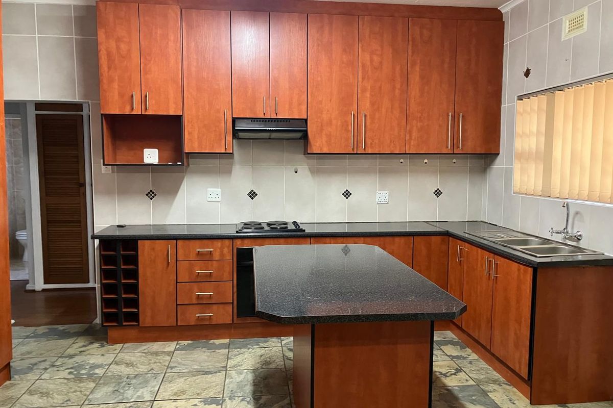 A functional kitchen featuring wooden cabinetry, granite countertops, a central island, built-in oven and hob, and tiled flooring throughout.