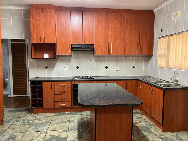 A functional kitchen featuring wooden cabinetry, granite countertops, a central island, built-in oven and hob, and tiled flooring throughout.