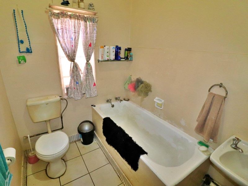 A functional bathroom featuring a standard bathtub, toilet, and washbasin, with tiled flooring and wall-mounted fixtures, currently requiring cosmetic updates.