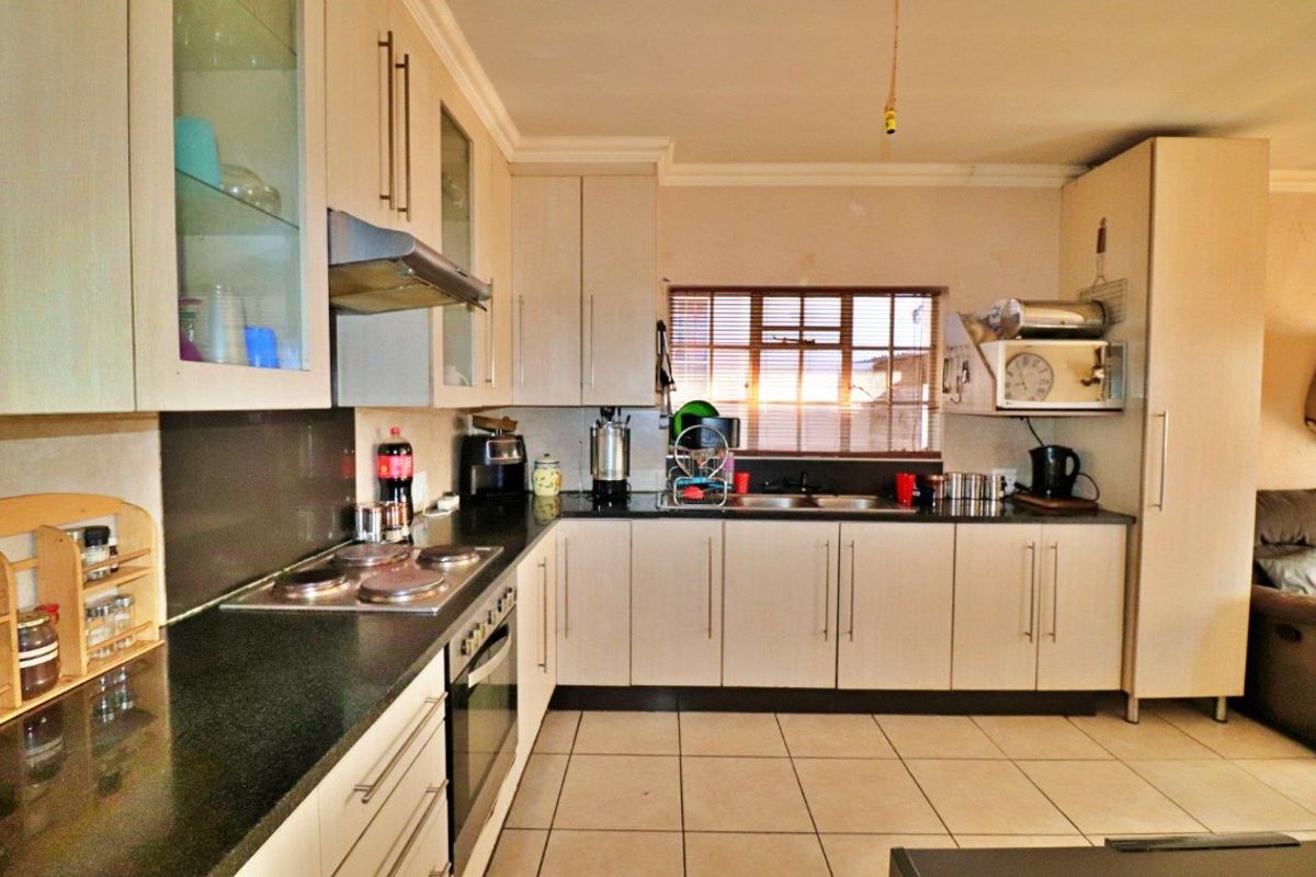 Functional kitchen featuring light-toned cabinetry, dark countertops, integrated oven and hob, and tiled flooring with a window providing natural light.