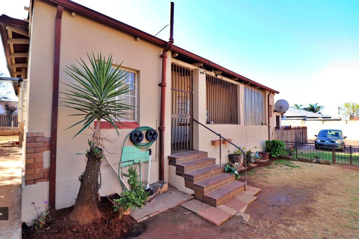 Rear exterior view of the house featuring brick steps, security bars on windows, and a basic garden area with a downpipe and external plumbing.