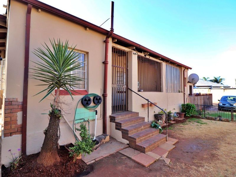 Rear exterior view of the house featuring brick steps, security bars on windows, and a basic garden area with a downpipe and external plumbing.