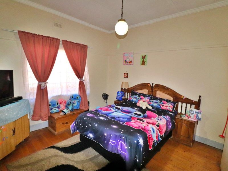A bedroom featuring original hardwood flooring, a picture rail, and a central pendant light fixture, offering a functional space with classic architectural details.