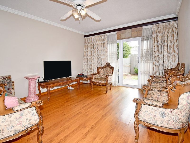 A living room featuring laminate flooring, crown molding, a ceiling fan, and a glass door providing access to the outdoor area.