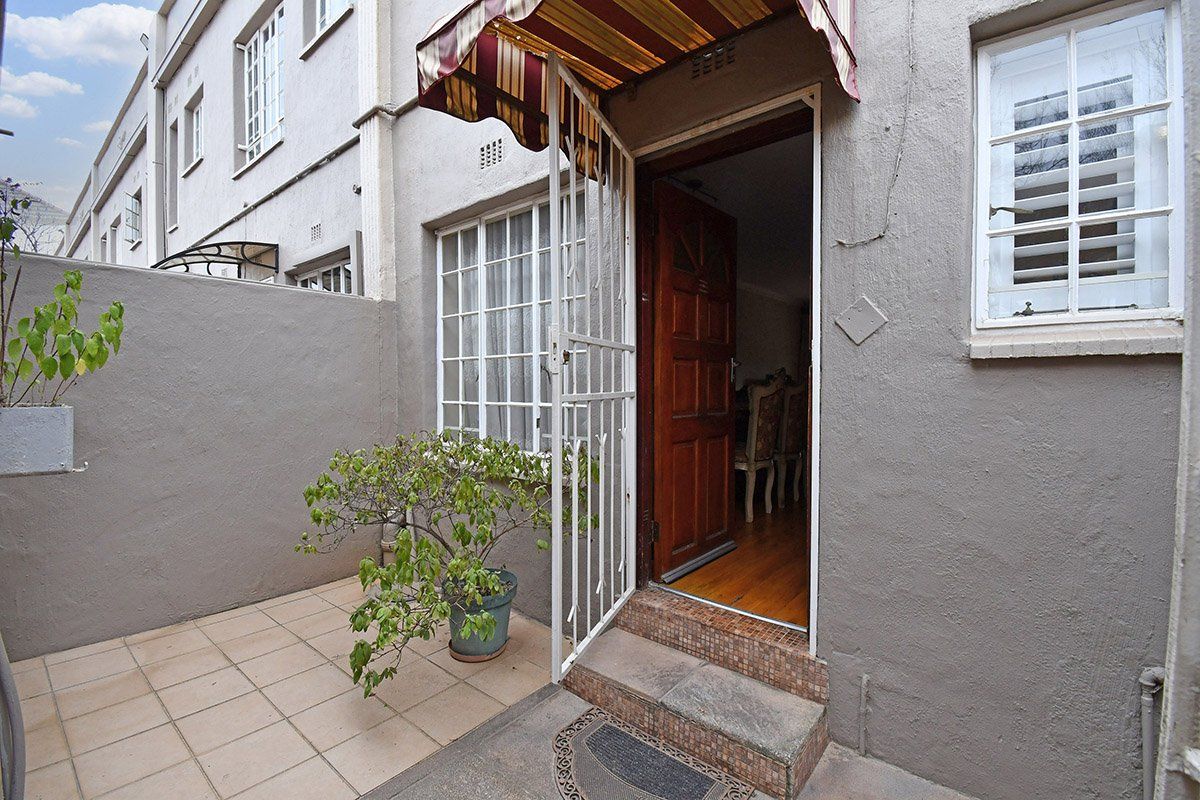 A rear exterior view of a townhouse featuring a small tiled patio, security gate, and a striped awning over the entrance.