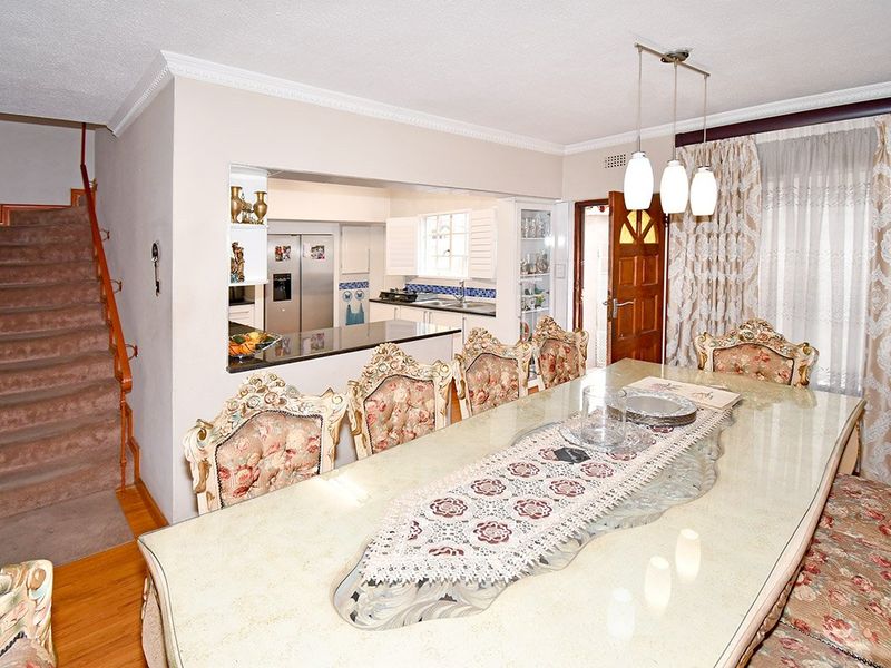 Open plan dining area featuring timber flooring, adjacent kitchen with granite countertops, and a staircase leading to the upper level.