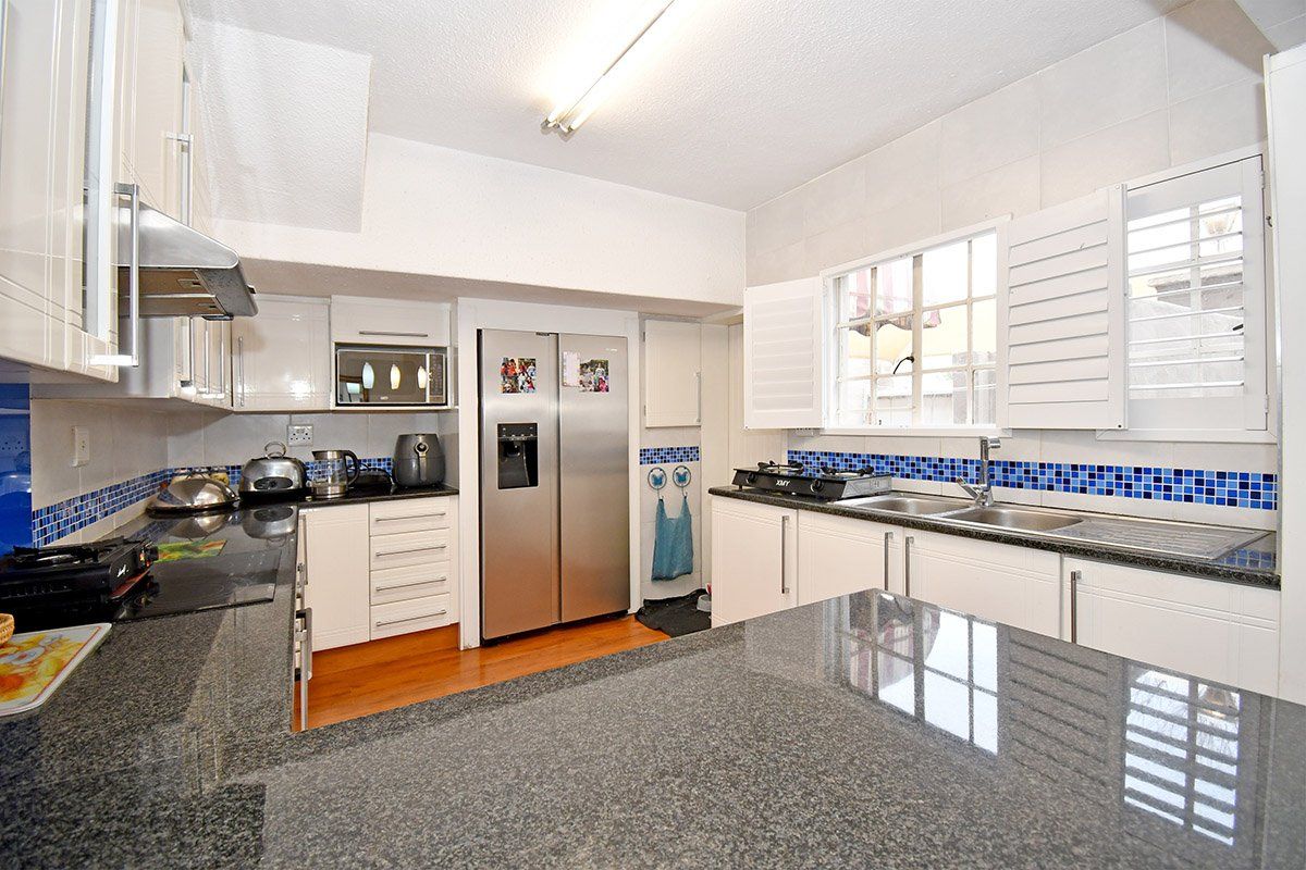 A functional kitchen featuring granite countertops, white cabinetry, a stainless steel double sink, and a tiled backsplash with integrated appliances.