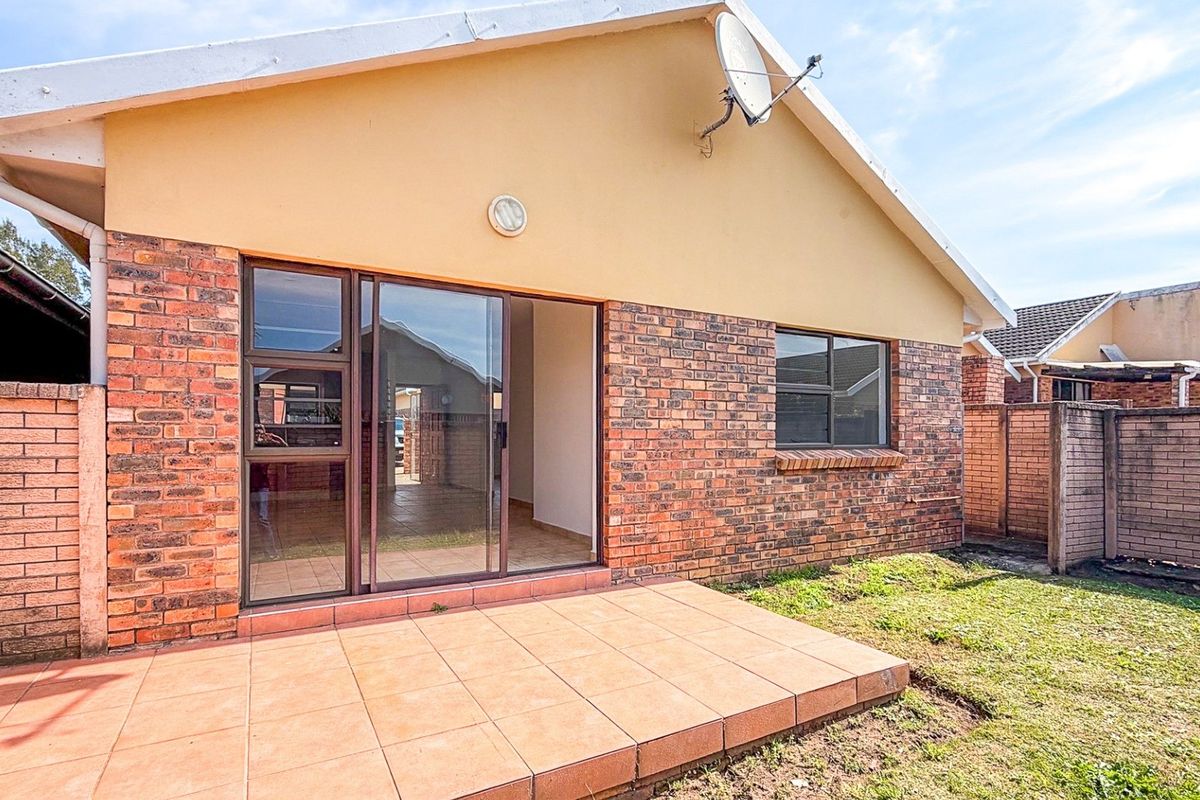 Rear view of the townhouse featuring a tiled patio, sliding glass door access, and a private garden area enclosed by brick boundary walls.