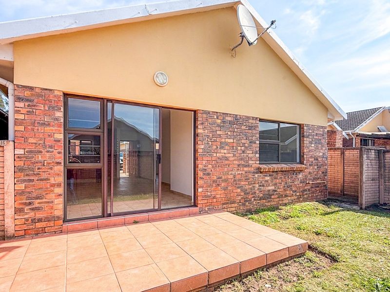 Rear view of the townhouse featuring a tiled patio, sliding glass door access, and a private garden area enclosed by brick boundary walls.