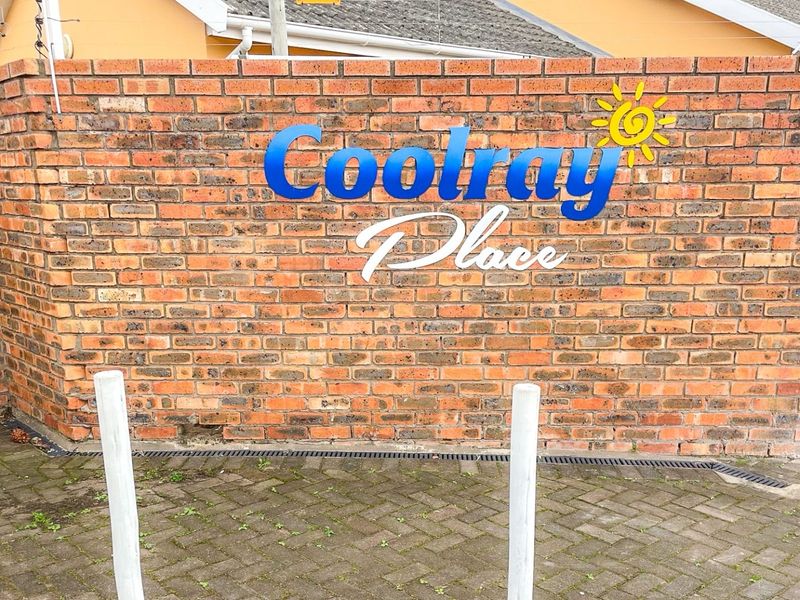 The entrance facade of Coolray Place featuring a prominent brick boundary wall with complex signage and paved driveway access.