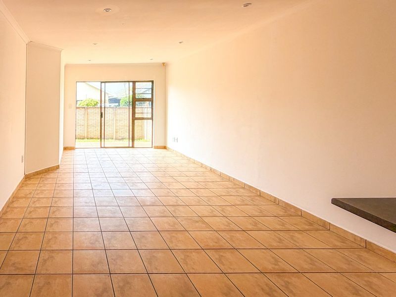 Spacious open-plan living area featuring neutral tiled flooring, recessed lighting, and a sliding glass door providing access to the rear exterior.