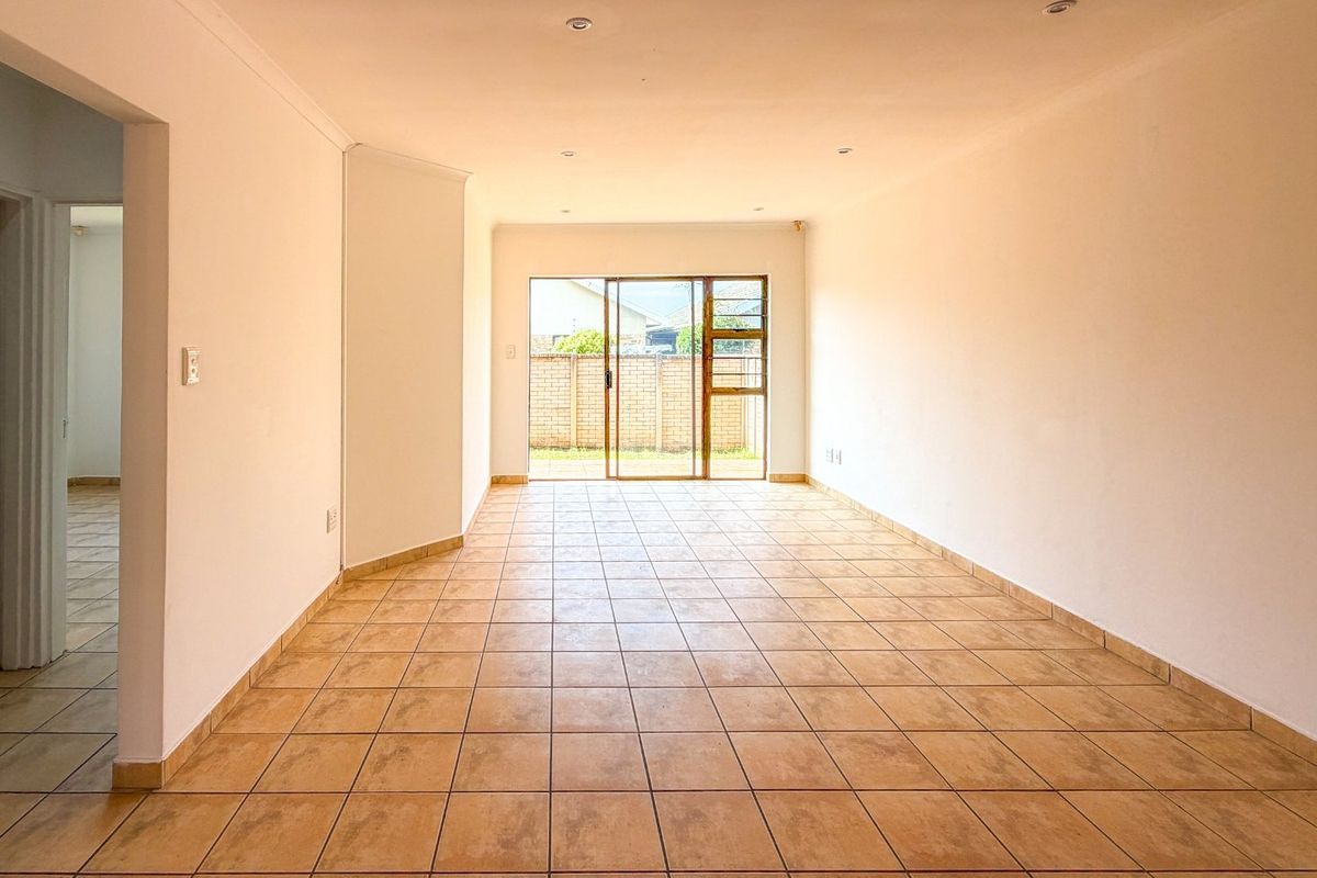 A spacious, empty living area featuring neutral tiled flooring, recessed lighting, and a sliding glass door providing access to the rear exterior.