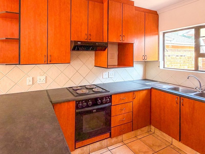 A functional kitchen featuring wooden cabinetry, dark laminate countertops, a built-in oven with hob, and a stainless steel double sink.