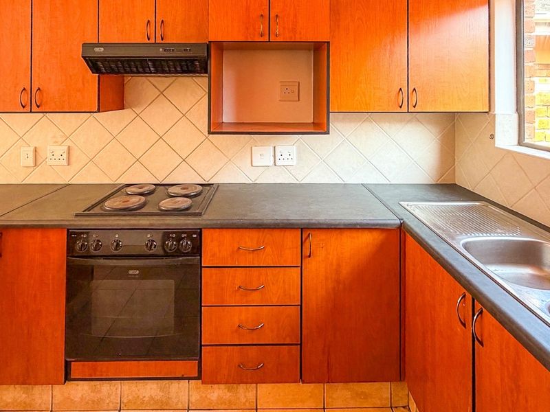 A functional kitchen featuring wood-finish cabinetry, dark laminate countertops, a built-in oven with hob, and a double stainless steel sink.