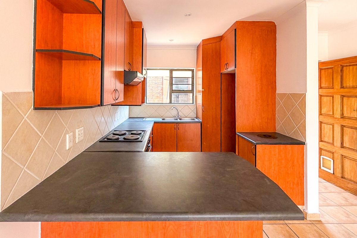 A functional kitchen featuring wooden cabinetry, dark laminate countertops, an electric hob, and a tiled backsplash, offering a practical layout for daily use.