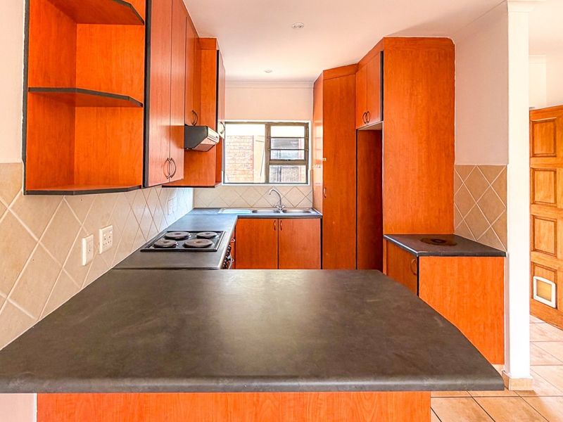 A functional kitchen featuring wooden cabinetry, dark laminate countertops, an electric hob, and a tiled backsplash, offering a practical layout for daily use.