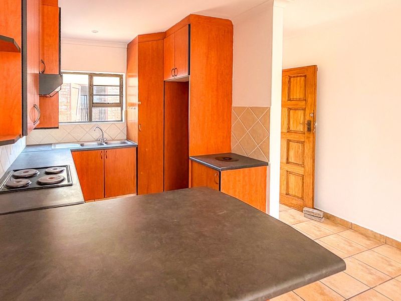 A functional kitchen featuring laminate cabinetry, dark countertops, a built-in hob, and tiled flooring, offering a blank canvas for modern updates.